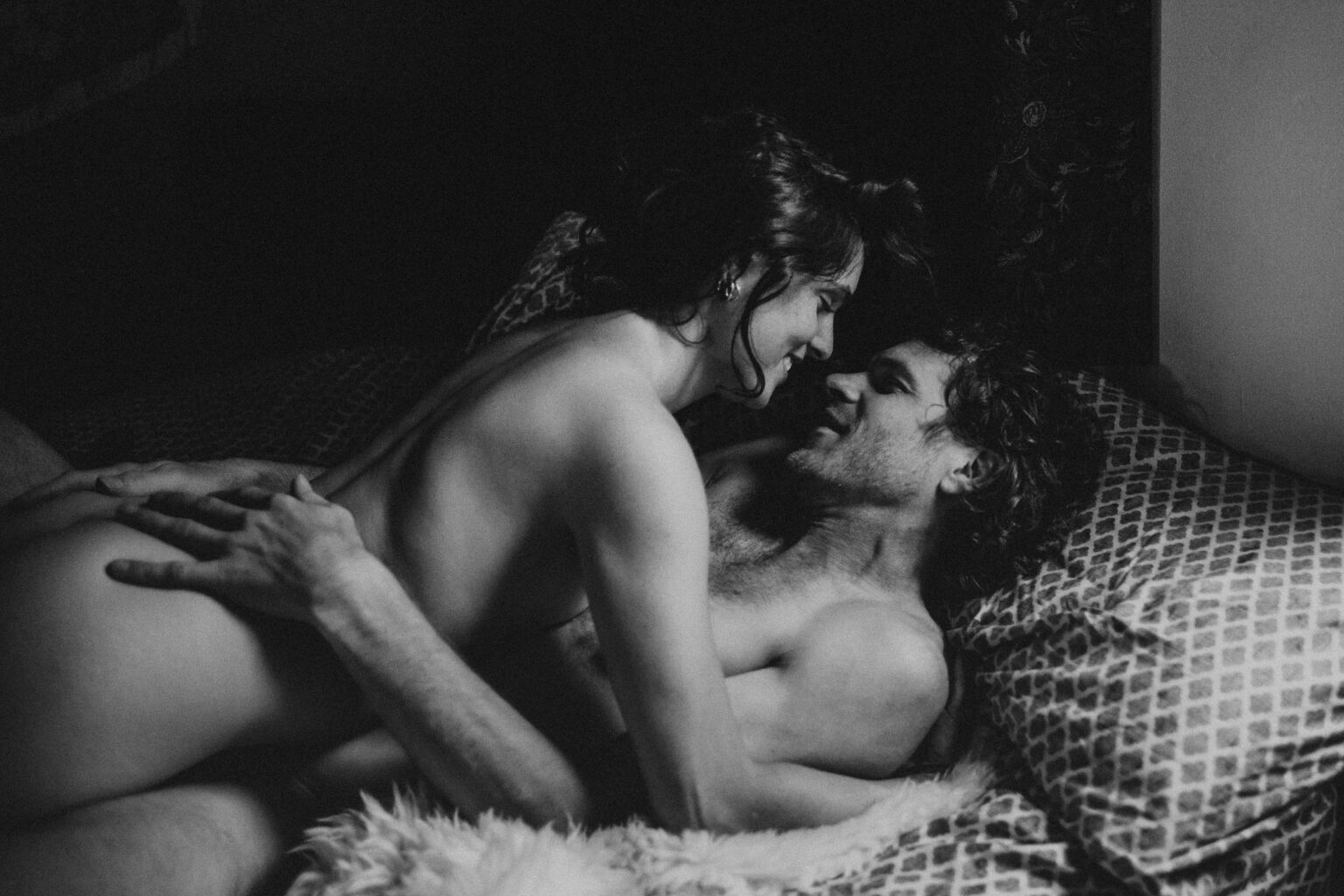 Black and white photo of couple rolling around in their bed during a home photo session. 