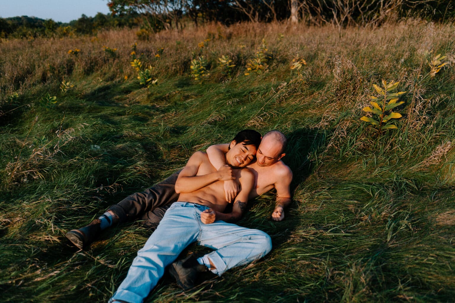 Gay couple laying in a field of tall grass shirtless holding each other in boudoir photography shoot in Toronto.